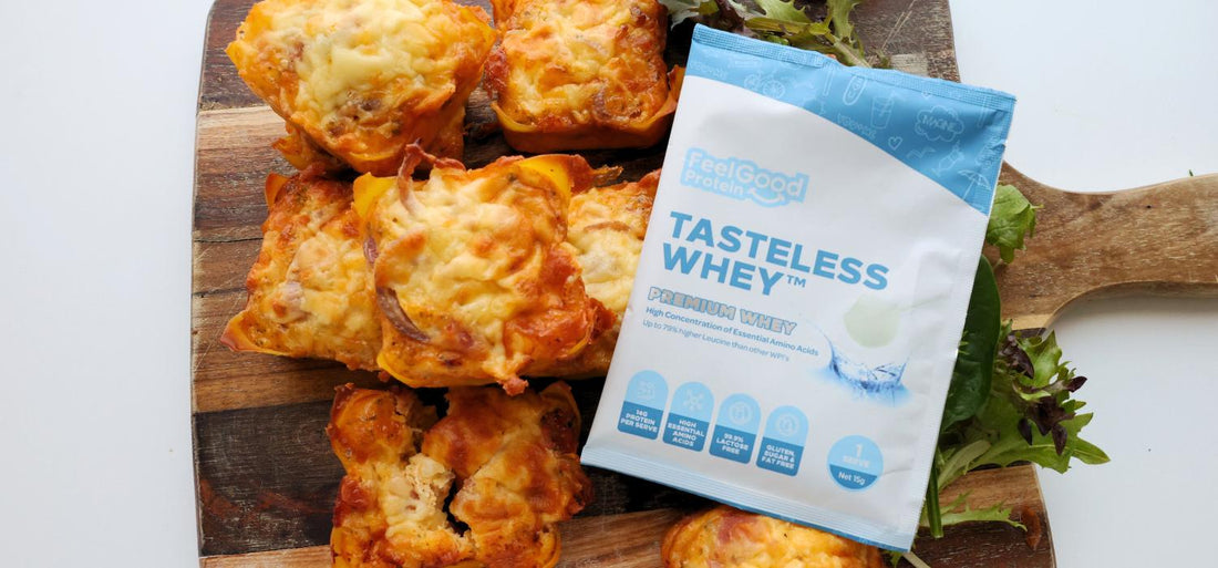Birds eye view photo of a sachet of Tasteless Whey by Feel Good Protein in the centre of a wooden board holding 7 Bacon & Onion Protein Bites with a softly blurred modern kitchen in the background. 