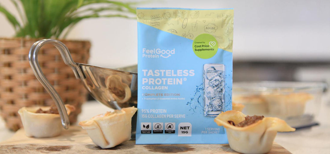 A close-up of three beef dumpling cups arranged on a wooden board, with a small silver sauce jug and a colourful Tasteless Protein Collagen sample packet beside them; a blurred plant sits in the background.
