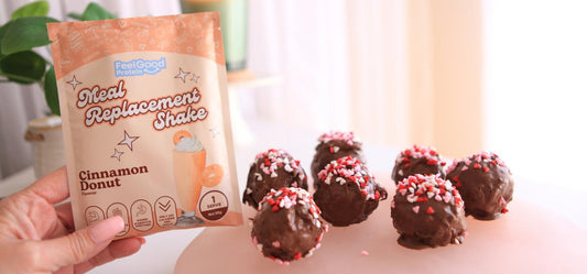Hand holding a yellow and blue sample packet reading Meal Replacement Shake by Feel Good Protein (Cinnamon Donut) next to 7 sprinkle and chocolate covered protein balls