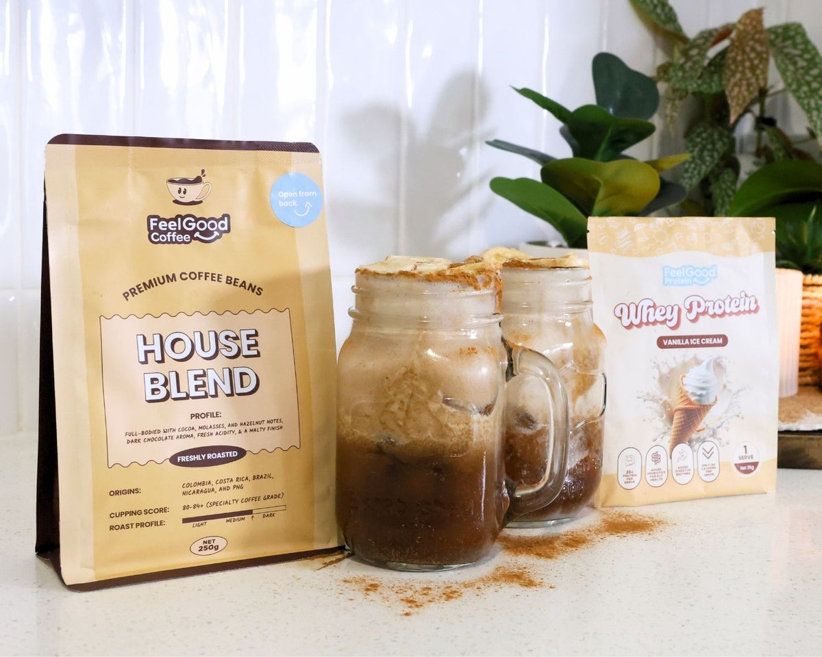 Gallery image of Banana Bread Protein Iced Latte recipe steps, showing a bag of House Blend Beans by Feel Good Coffee, two cups of Banana Bread Protein Iced Lattes, to the left of a yellow sachet of Whey Protein by Feel Good Protein (Vanilla Ice Cream). 