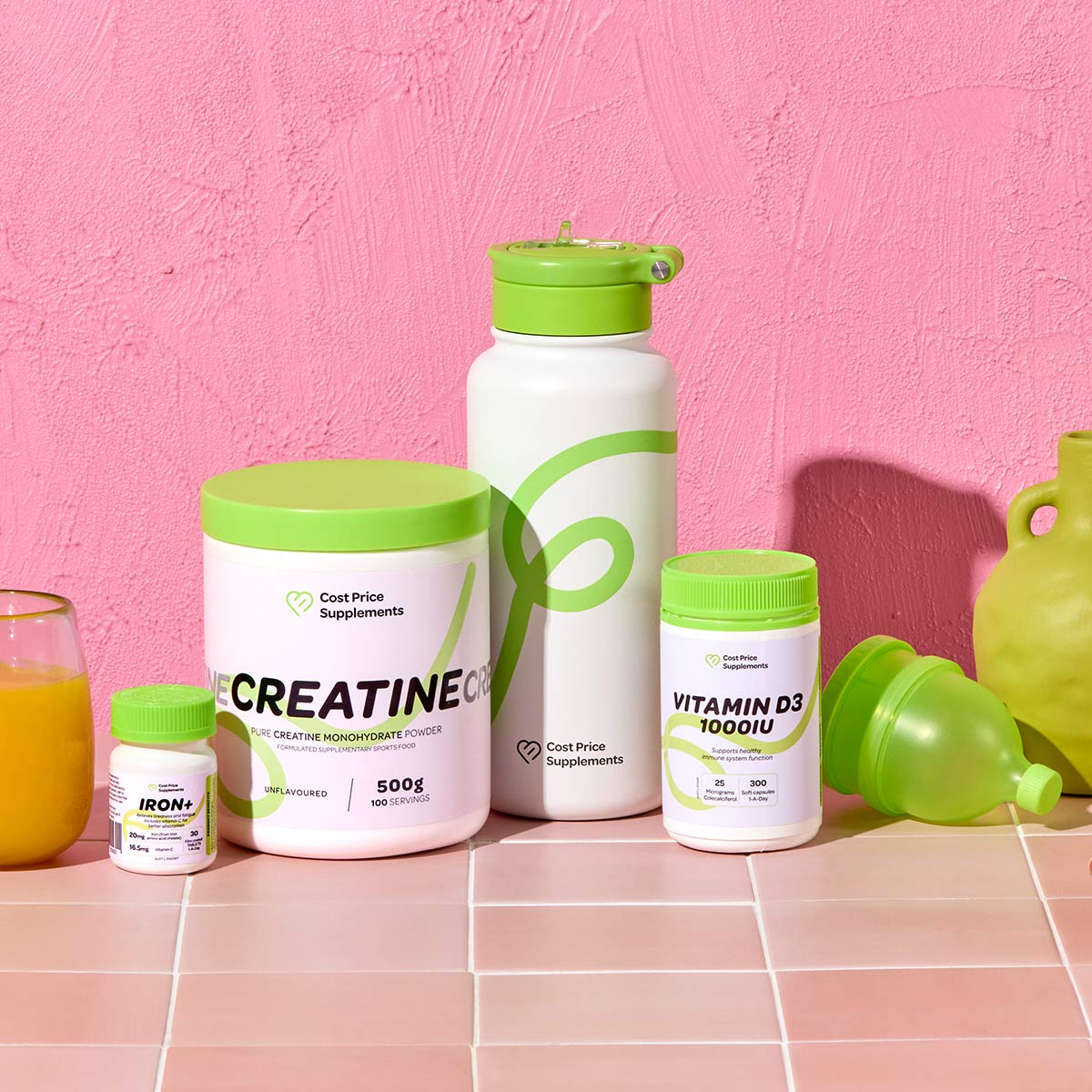 Supplement products including creatine, vitamin D3, water bottle, and iron supplements on a pink background.