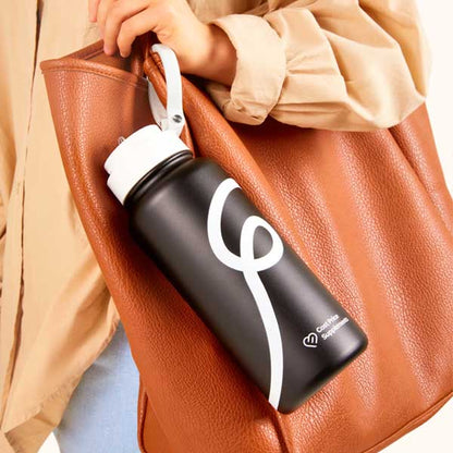 Black water bottle with a white swirl clipped onto a brown bag held by a women.