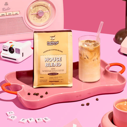 House Blend by Feel Good Coffee next to an iced latte on a pink table