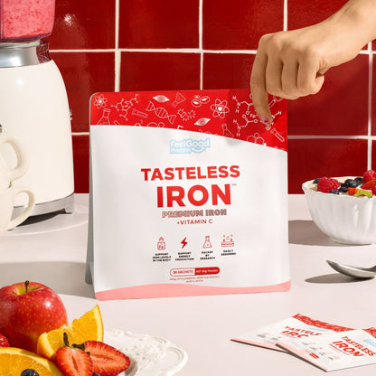 Tasteless Iron by Feel Good Protein in front of red tiled wall and next to fruit bowl